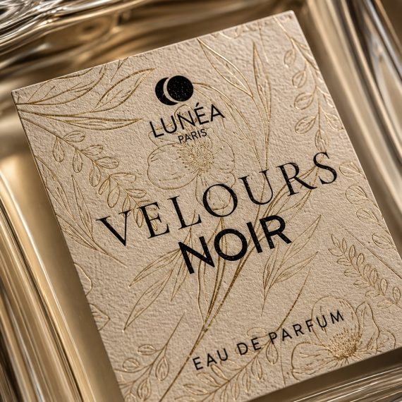 Gros plan sur l'étiquette texturée du flacon Velours Noir avec finitions dorées, illustration florale et design de packaging parfum premium.